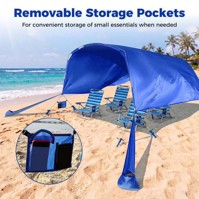 Blue beach tent with removable storage pockets on a sandy beach with ocean and palm trees in the background.